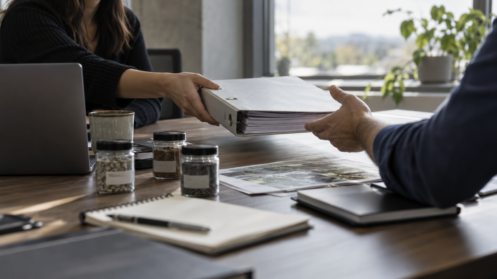 Two people at a table exchanging a binder of production documents